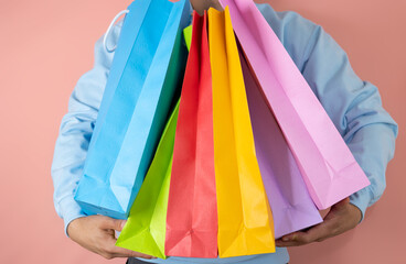 Unrecognizable man wearing a blue sweatshirt holds numerous multicolored shopping bags in both...
