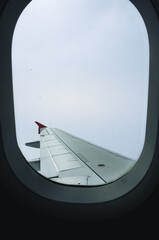 Airplane wing with overcast and gloomy sky in the background seen from passenger view through the window. Air travel concept.