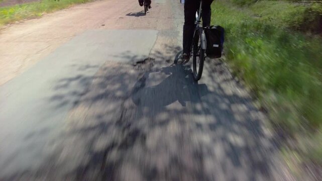 Sporty people riding bicycle, shadows on asphalt road, closeup photo. Cyclist with pannier bag biking on patchy road. Shadow play, movement and sunny journey