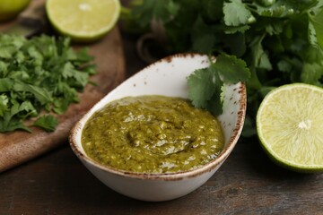 Tasty sauce with cilantro and limes on wooden table, closeup