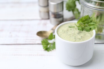 Tasty cilantro sauce in bowl on white wooden table, closeup. Space for text