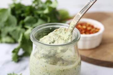 Taking tasty cilantro sauce with spoon from jar at light table, closeup