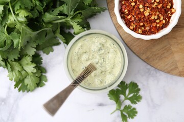 Tasty cilantro sauce in jar and spices on light marble table, flat lay