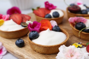 Sweet tartlets with berries and flowers on grey table, closeup. Delicious dessert