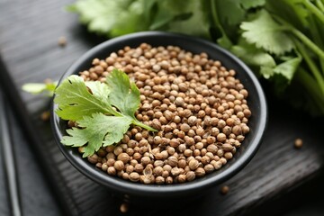 Coriander seeds and fresh cilantro leaves in bowl on dark table, closeup