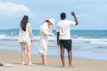 Group of diverse friends having fun at the beach, running and splashing in the waves on a sunny day