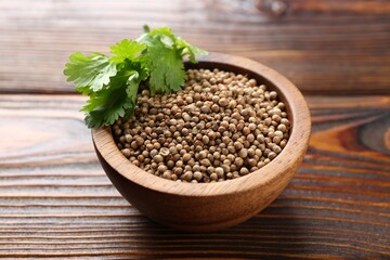 Coriander seeds and fresh cilantro leaves in bowl on wooden table, closeup