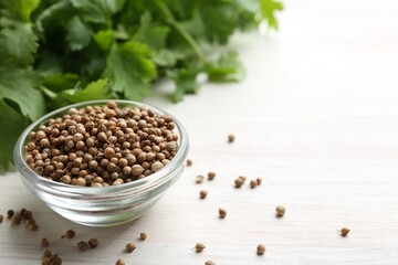 Coriander seeds in bowl and fresh cilantro leaves on light wooden table, closeup. Space for text
