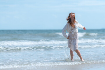 Portrait of young woman enjoying a playful walk on the beach as splash through the waves