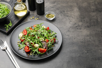 Tasty salad with arugula, mozzarella and vegetables served on grey table, closeup. Space for text