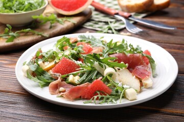 Tasty salad with arugula, prosciutto, cheese, pear, grapefruit and nuts on wooden table, closeup