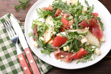 Tasty salad with arugula, prosciutto, cheese, pear, grapefruit and nuts on wooden table, above view