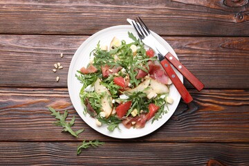Tasty salad with arugula, prosciutto, cheese, pear, grapefruit and nuts on wooden table, top view