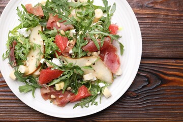 Tasty salad with arugula, prosciutto, cheese, pear, grapefruit and nuts on wooden table, top view