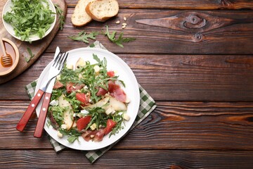 Tasty salad with arugula and prosciutto served on wooden table, flat lay. Space for text