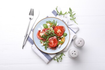 Tasty salad with arugula, cheese, tomatoes, nuts and prosciutto on white wooden table, flat lay