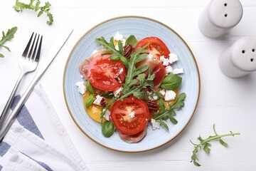 Tasty salad with arugula, cheese, tomatoes, nuts and prosciutto on white wooden table, flat lay