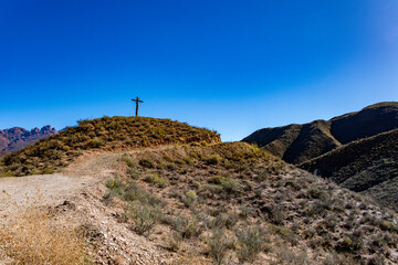 Fototapeta premium A solitary cross stands atop a grassy hill overlooking the vast mountains of Valle de Luracatao.