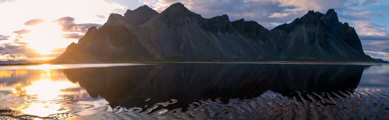 Golden rays of sunset illuminate the rugged peaks of Stokksnes Mountain, creating a stunning...