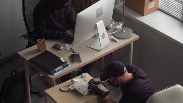 High angle shot of male criminal installing bugging device into desktop telephone spying on confidential corporate data with partner hacking into computer in office room