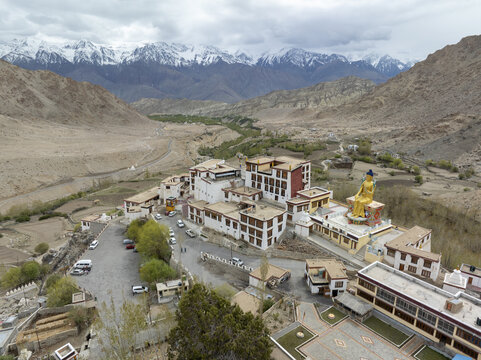 Aerial view of the serene Diskit Monastery, with its golden Maitreya Buddha statue gazing over the Nubra Valley, framed by the snow-capped Himalayas, Leh, Ladakh, India.