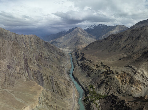 Aerial view of the Indus River snaking through rugged, sun-kissed mountains under a vast sky, the river contrasting with the arid landscape, Leh, Ladakh, India.