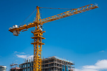 Construction site showcases a towering crane operating above a multi-story building under development in a bright, clear sky