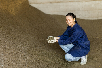 Asian woman farmer takes handful of granulated feed in palm of hand, checks purity and absence of...