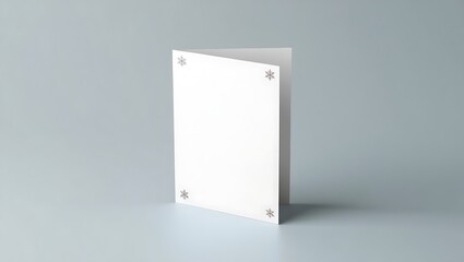 A white greeting card with snowflake decorations standing on a light gray surface in a studio shot