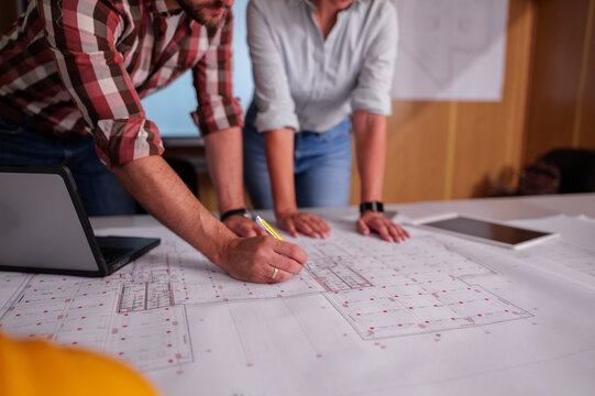Two architects are examining blueprints and discussing a project during a productive meeting in their office, collaborating on design details and project specifications