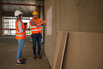 Two construction workers. A man and a woman wearing safety vests and helmets. Are discussing a...