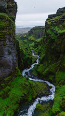 Majestic cliffs rise sharply over a meandering river in Mulagljufur Canyon, Iceland. Lush green...