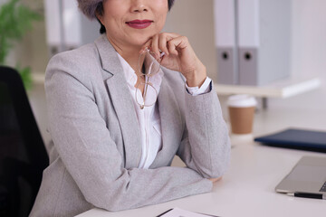 Experienced Asian businesswoman holds reading glasses pondering business strategy career growth...