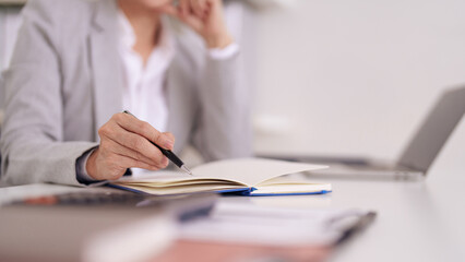 Adult professional hand writing notes in a notebook at an office desk with a laptop visible for business strategy job application preparation