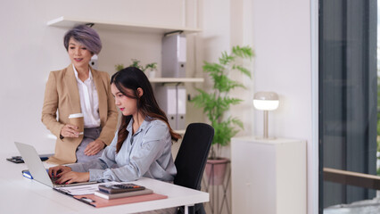 Asian female executives guide young professional collaborating on laptop business strategy in...