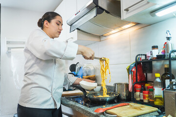 Chef using tongs to serve pasta in a modern kitchen