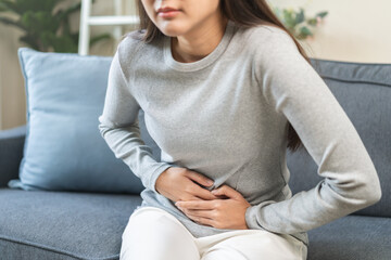 Sick asian young woman in pain, hand holding belly, stomach pain from food poisoning, girl hurt...