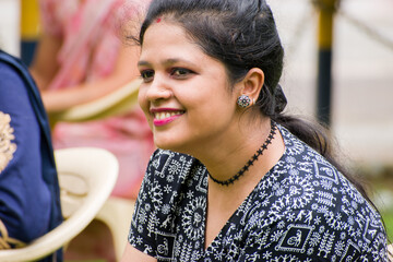 young Indian woman smiling gracefully, wearing a traditional black and white Warli print top paired...