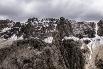 Snow dusted cliffs under heavy skies — aerial shot of the Sella Group in the Dolomites, with...