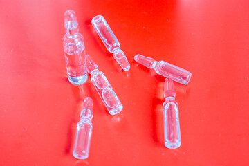 Transparent medical ampoules with liquid contents, arranged on a vibrant red background, form a...