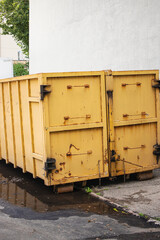 Industrial yellow dumpster sits beside a concrete wall in an urban setting on a bright sunny day