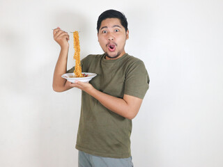 handsome asian man is enjoying noodles with a fork and showing a shocked face
