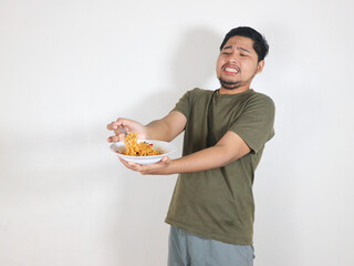 Handsome Asian man holding noodles and showing a refusal pose by pushing the noodles away with a...