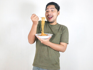Handsome Asian man enjoying noodles with a fork with an expression of being very tempted by the...