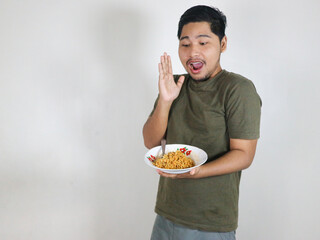 Handsome Asian man holding a plate of fried noodles and showing a surprised expression. Eating...