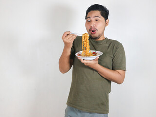 Handsome Asian man enjoying noodles with a fork with an expression of being very tempted by the...
