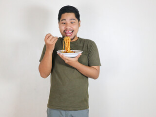 Handsome Asian man enjoying noodles with a fork with an expression of being very tempted by the...