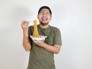 Asian handsome man holding a plate of noodles with a fork while showing a sad expression. bored...