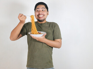 Handsome Asian man enjoying noodles with a fork with an expression of being very tempted by the...