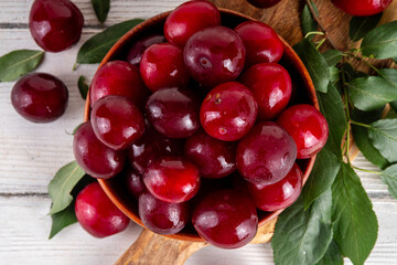 Fresh raw ripe cherry plum with leaves. Bowl of tasty farm bright red cherry plum fruits, in wooden craft bowl on white wooden background copy space